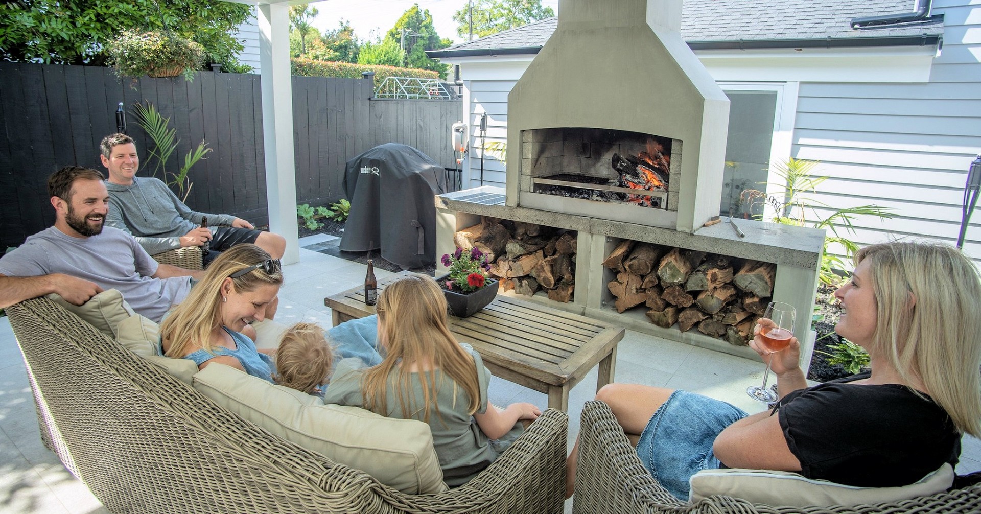 Picture of family and friends sitting on outdoor furniture around a Flare Fire Premier fireplace with a fire.